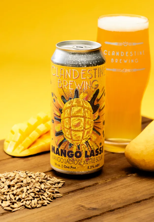 Can and glass of Clandestine Brewing Mango Lassi mango lactose kettle sour with fresh mango on a wooden table